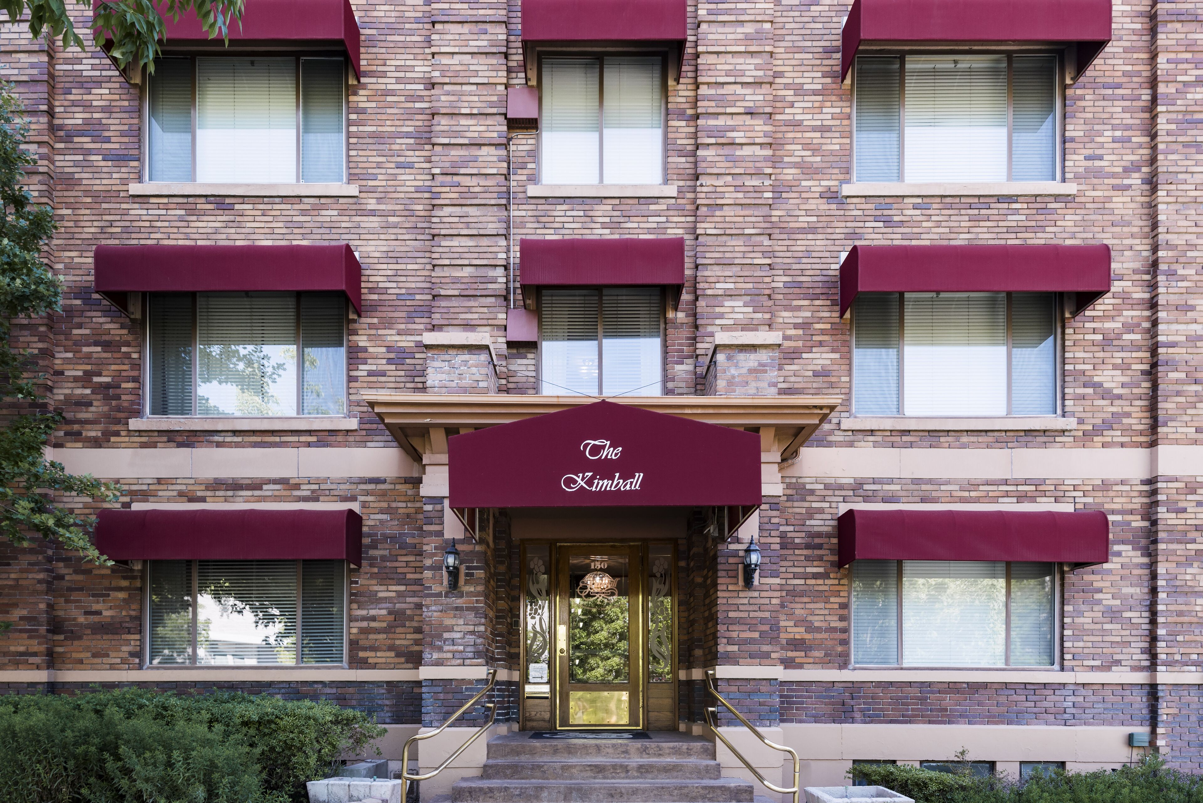 A multi-story building with a brick facade, a central entrance with a gold door, and a sign reading "The Kimball."