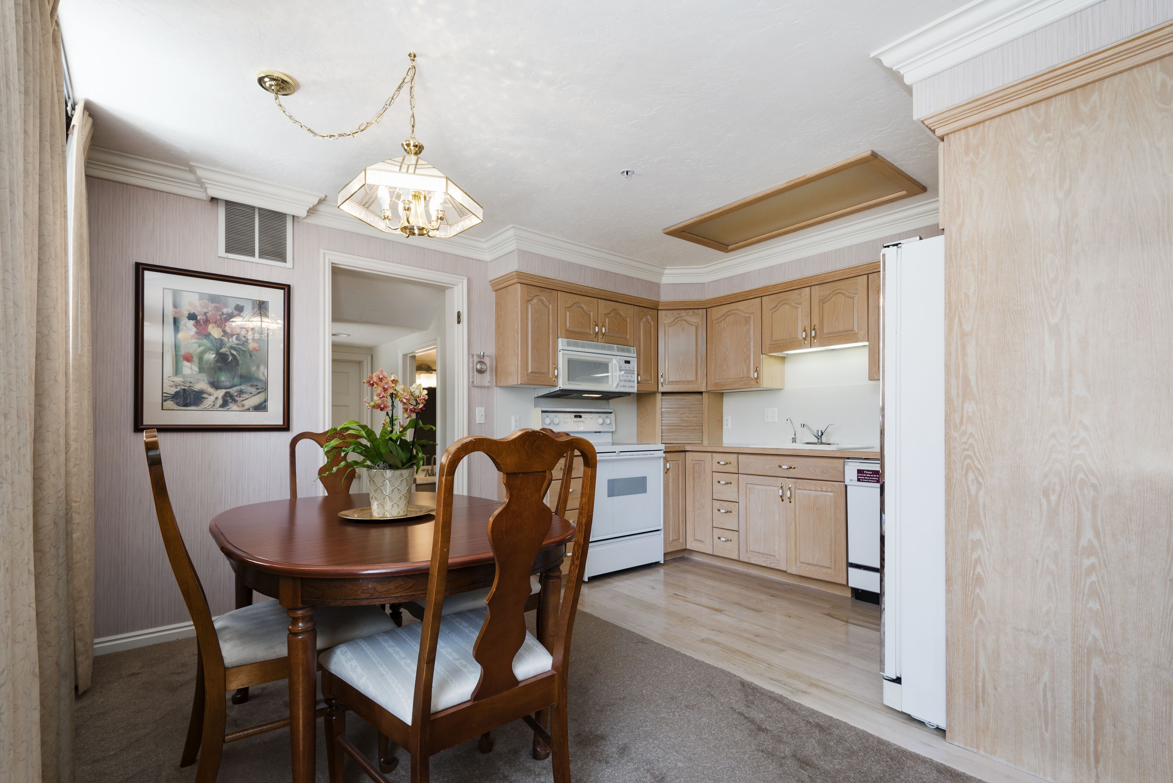 A dining area with a wooden table and chairs, a chandelier, and a microwave in the kitchen area.