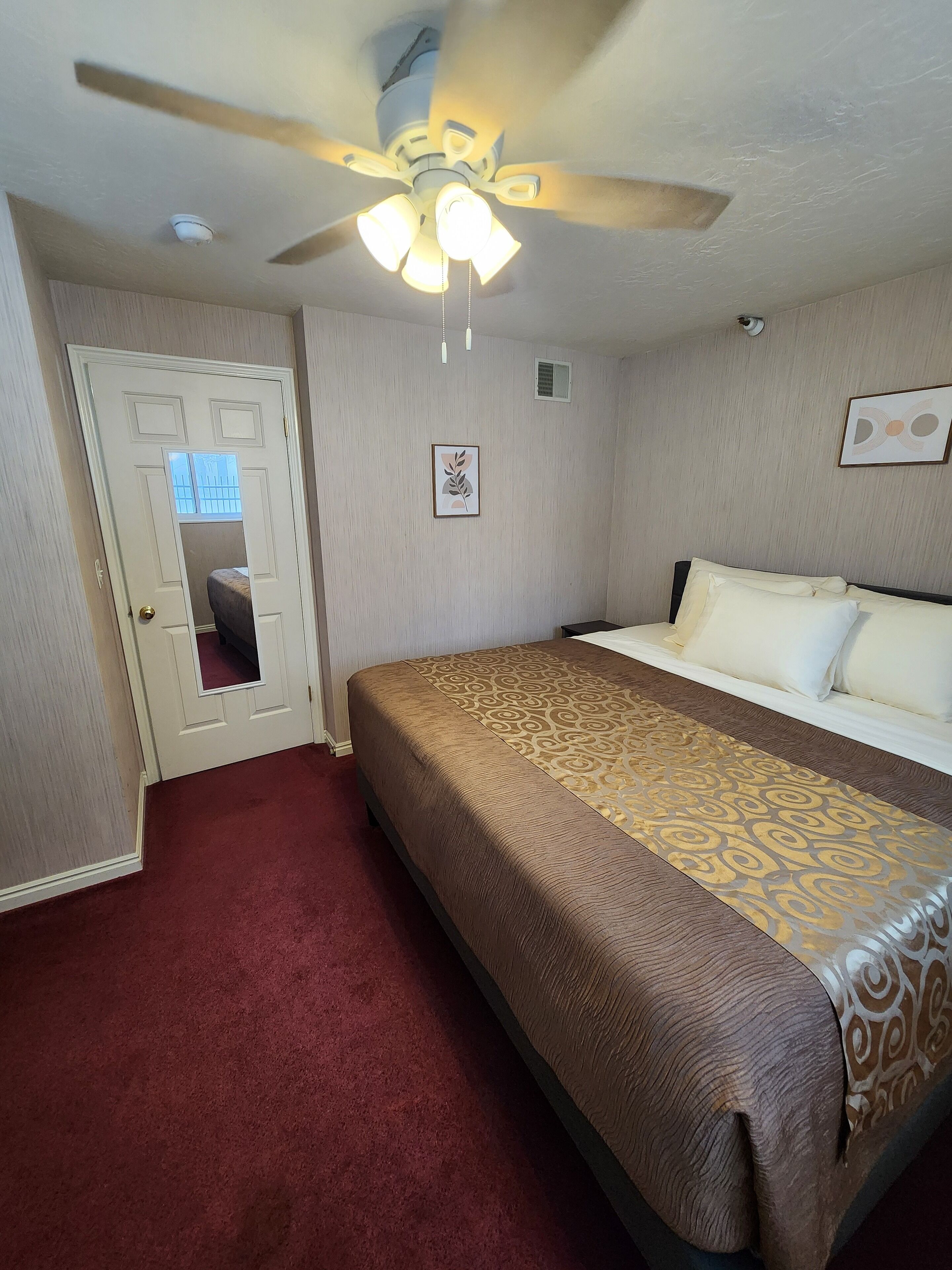 Ein Hotelzimmer mit Bett, Deckenventilator, Tür und kleinem Fenster.