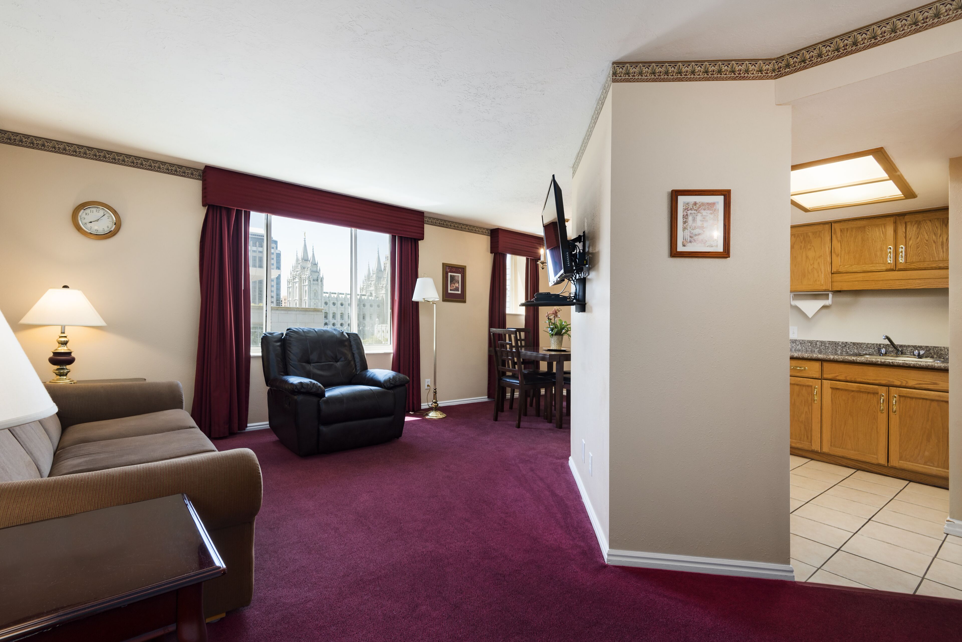 Habitación de hotel con sala de estar, una mesa de comedor, un sillón de cuero negro, un televisor de pantalla plana y un área de cocina.