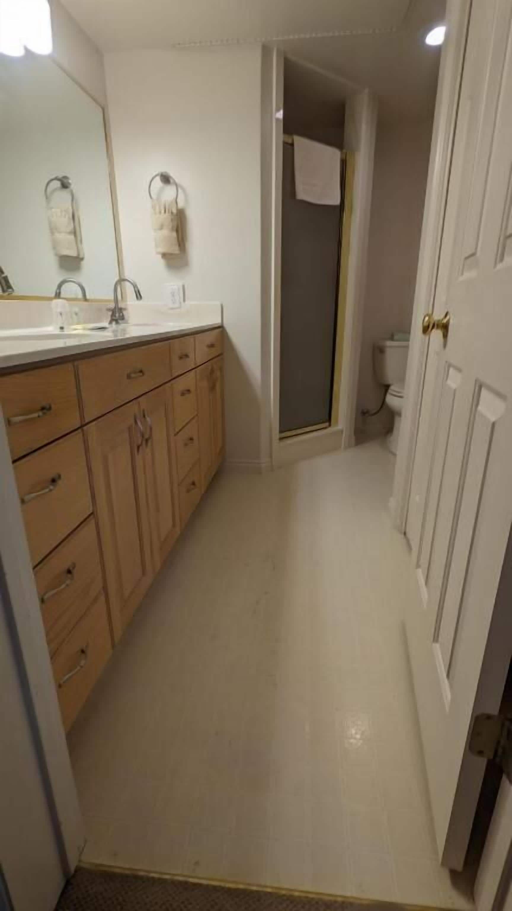 A bathroom with a wooden vanity, a mirror, a towel rack, and a shower area.