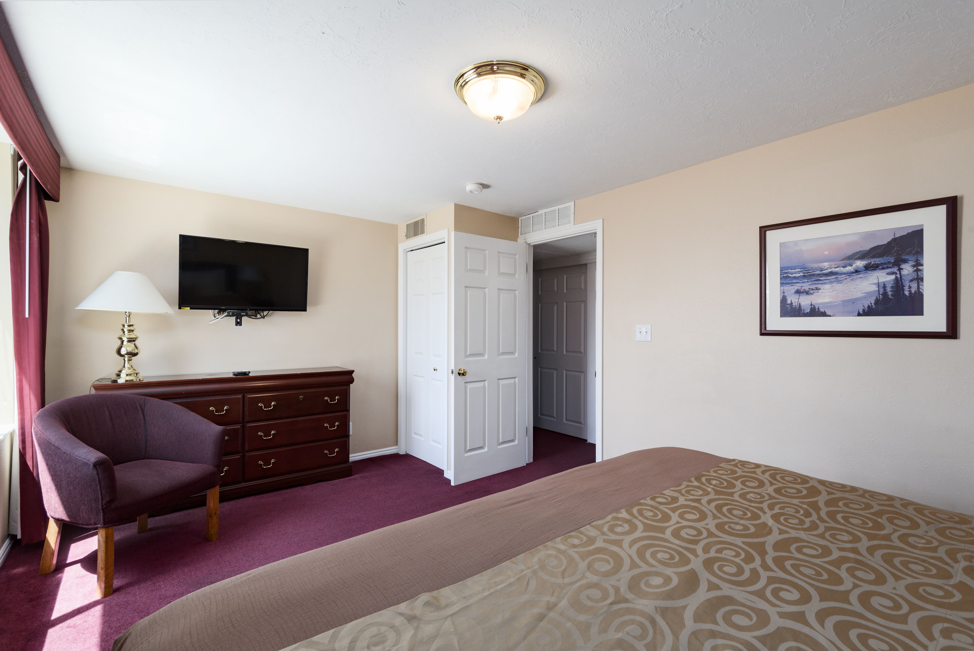 A hotel room with a bed, a television, a dresser, a chair, and a door leading to another room.