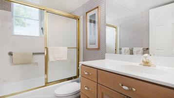 A bathroom with a bathtub, toilet, vanity with drawers, a mirror, and a towel rack.