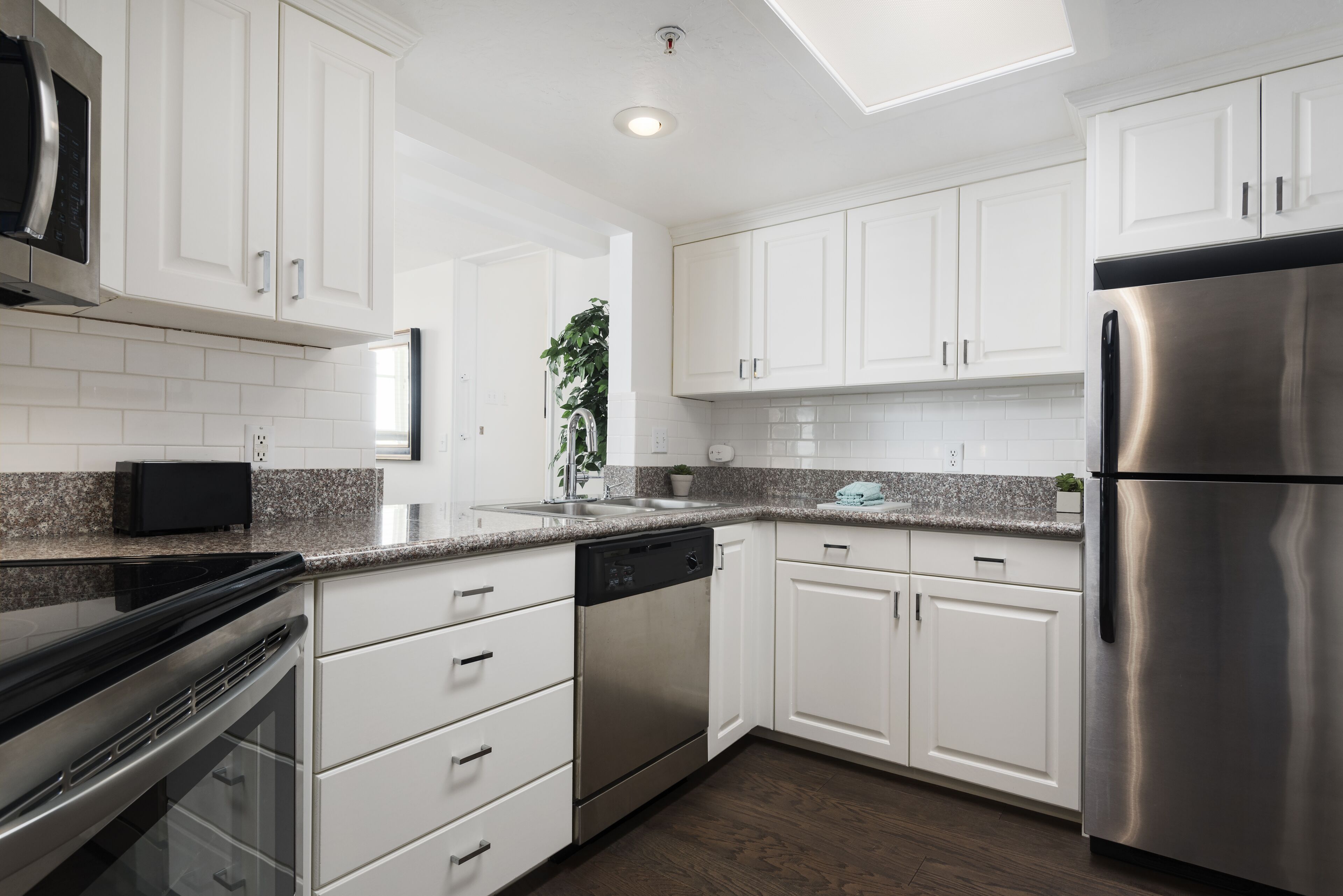 Una cocina moderna con armarios blancos, electrodomésticos de acero inoxidable, encimeras de granito y un tragaluz.