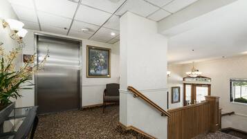A hotel lobby with a carpeted floor, a reception desk, a chair, a staircase, and a framed picture on the wall.