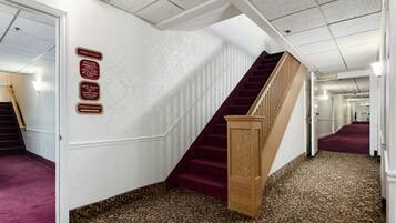 Pasillo de hotel con piso alfombrado, una escalera de madera y señales indicativas para el primer piso, incluyendo un gimnasio.