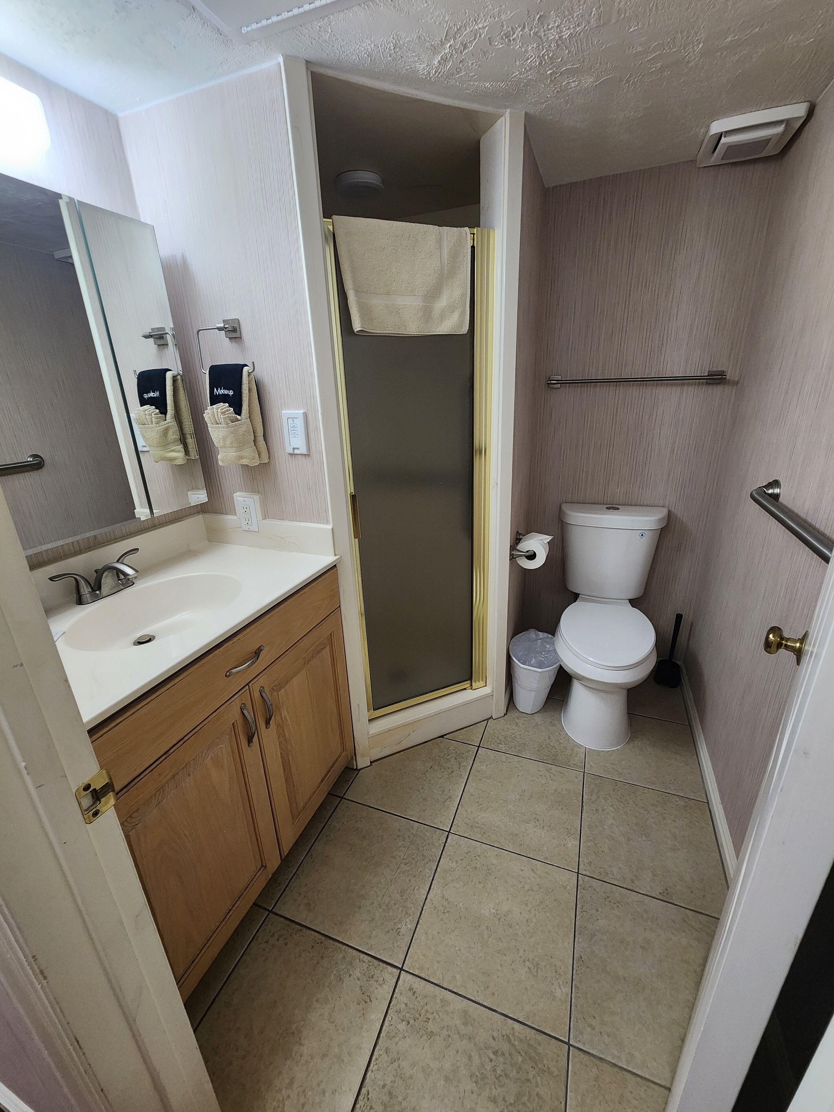 A bathroom with a sink, mirror, towel rack, toilet, and shower.