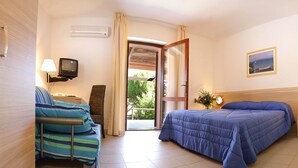 A hotel room with a bed, a chair, a TV, and a window with a view of greenery. - Hotel Club Mezzaluna (Carloforte)