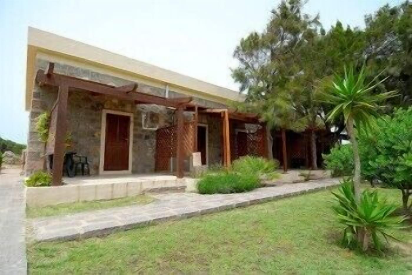 A two-story building with a stone facade, a covered porch, and a small garden area with a palm tree.