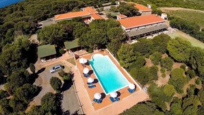 An aerial view of a resort with a swimming pool, lounge chairs, and a view of the ocean. - Hotel Club Mezzaluna (Carloforte)