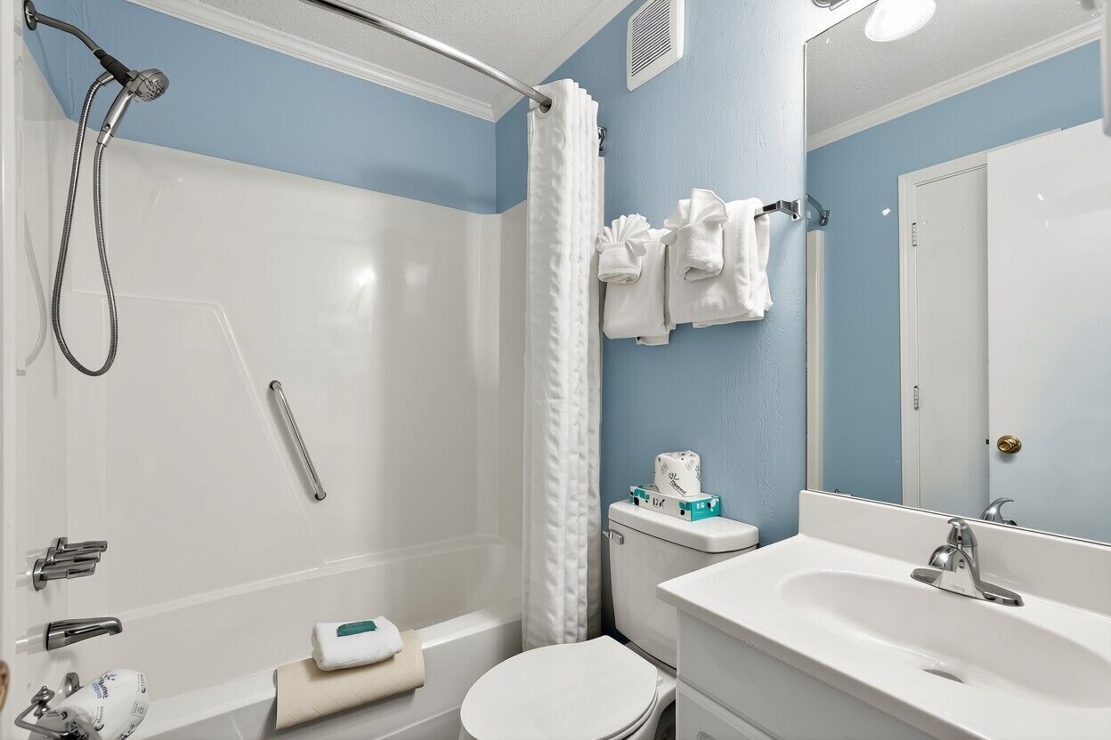 A bathroom with a shower, toilet, sink, and a mirror.