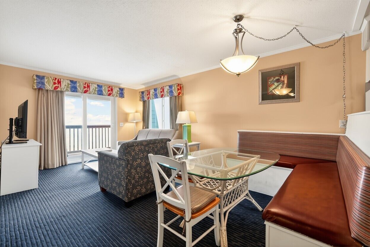 A hotel room with a sofa, a glass table with chairs, a TV, and a window with curtains.