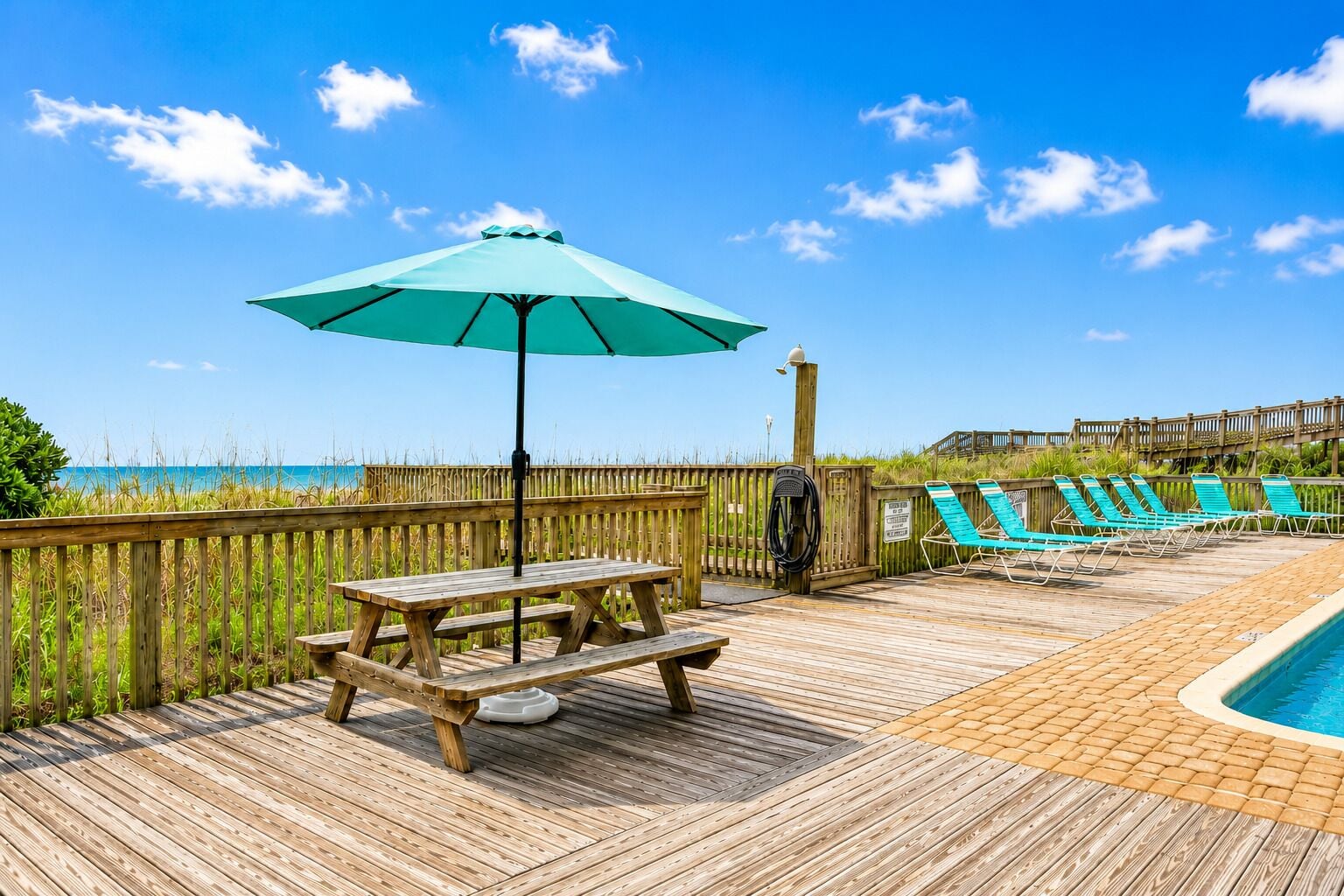 A wooden deck with a picnic table and umbrella, a pool with lounge chairs, and a wooden fence.