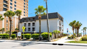 A multi-story hotel with balconies, palm trees, and a pedestrian crossing sign. - Ocean Forest Colony (Myrtle Beach)