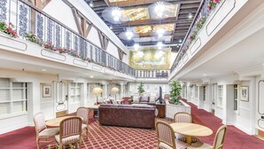 A spacious atrium with a high ceiling, ornate railings, and a central seating area with a red patterned carpet. - Plaza Suites Downtown New Orleans (New Orleans)