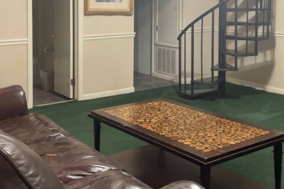 Una habitación con un sofá de cuero marrón, una mesa cubierta con objetos circulares, un cuadro en la pared y una escalera de caracol.