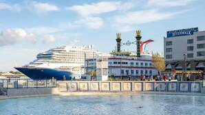 A cruise ship docked near a waterfront with a building labeled "Outlet Collection Riverwalk" in the background. - Plaza Suites Downtown New Orleans (New Orleans)