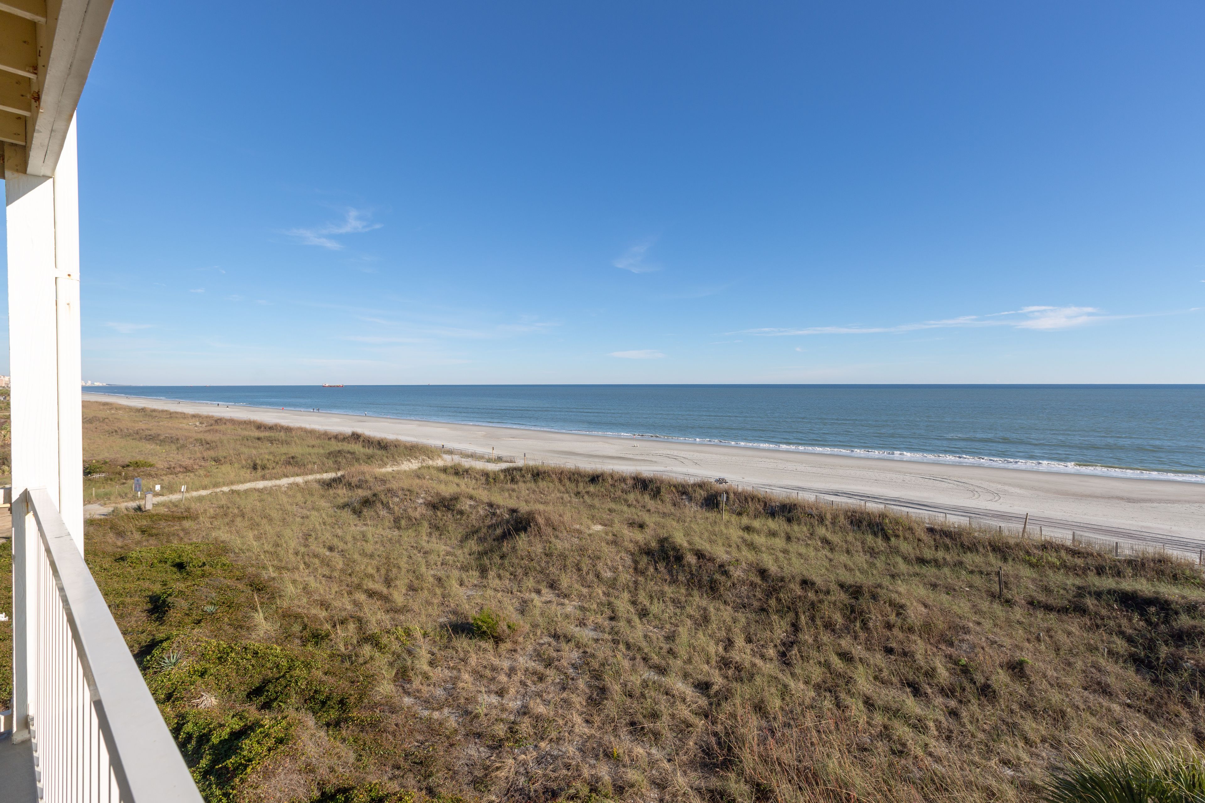 Une vue sur la côte, prise depuis un balcon donnant sur une plage, avec un ciel dégagé.