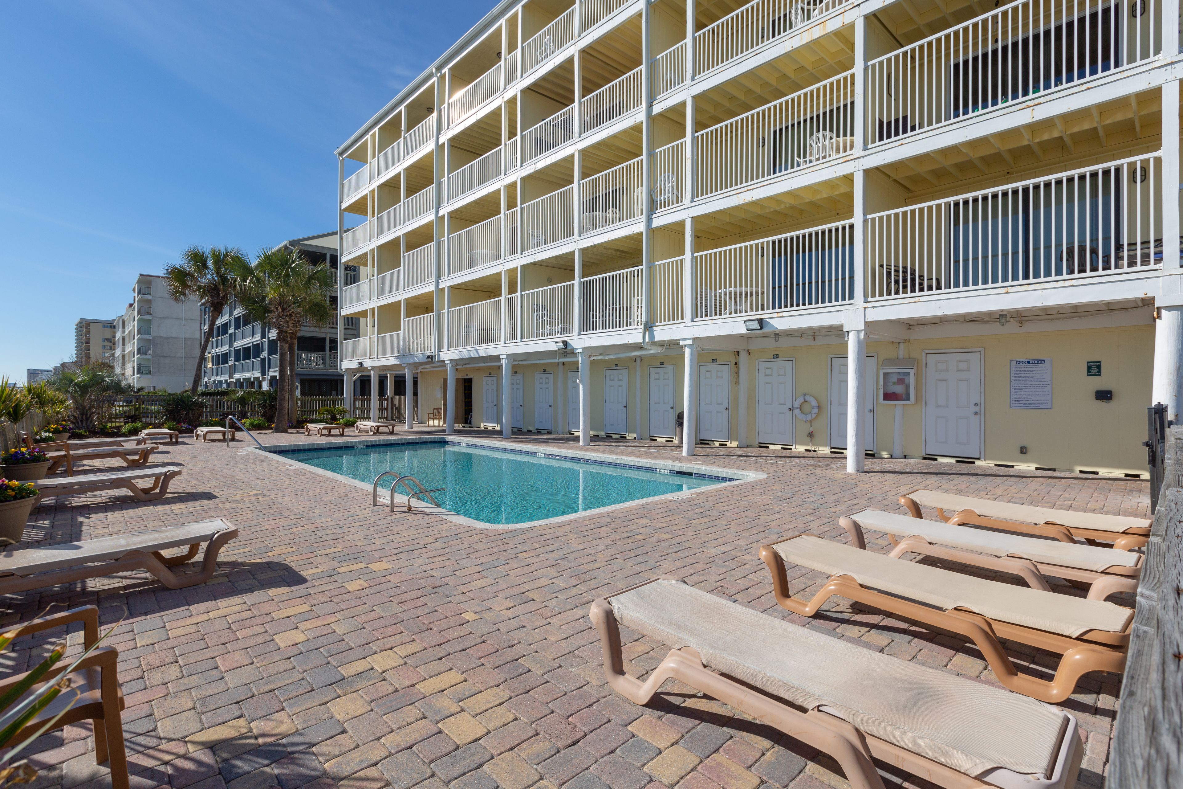 A hotel with a pool, multiple balconies, and lounge chairs.