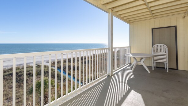 A covered balcony with a view of the ocean, a white chair, and a table. - Windy Shores II (North Myrtle Beach)