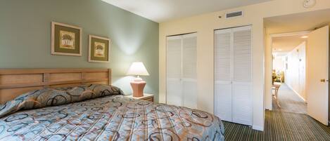 A hotel room with a large bed, a nightstand with a lamp, two framed pictures on the wall, and a closet with sliding doors.
