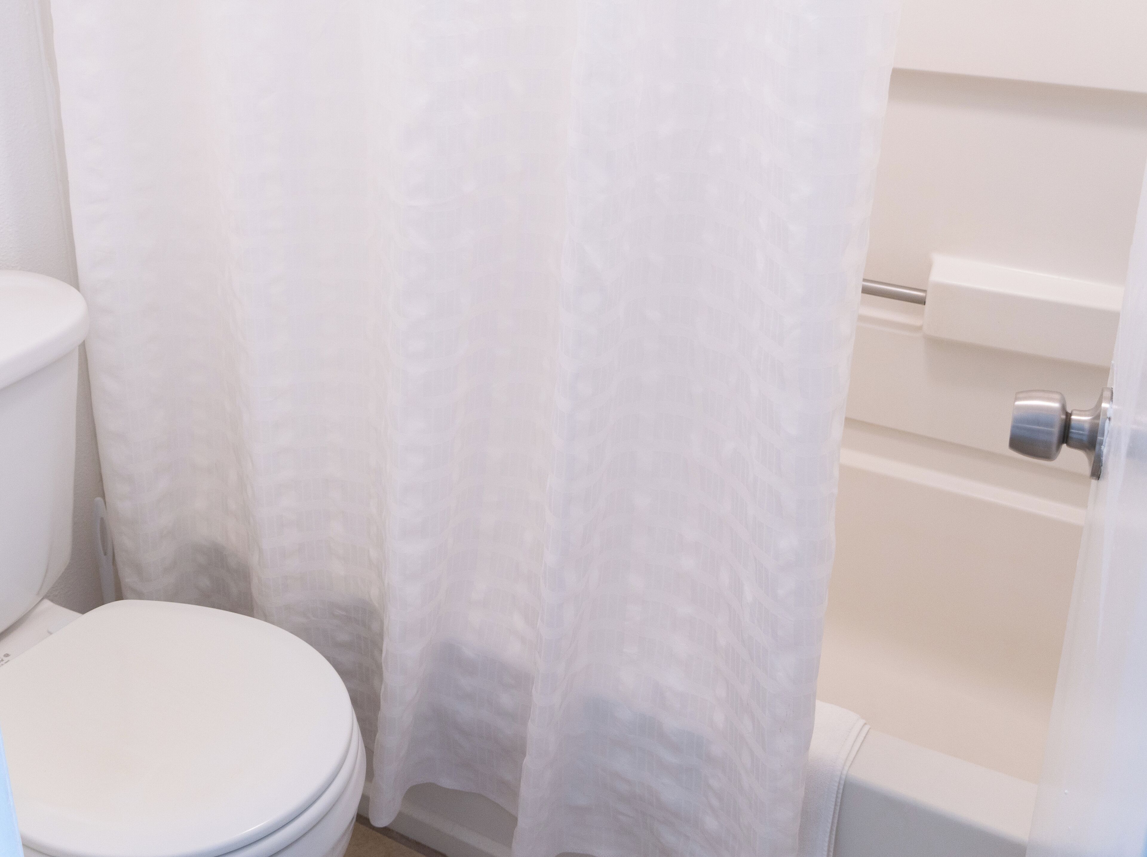 Een badkamer met toilet, douchegordijn en bad.