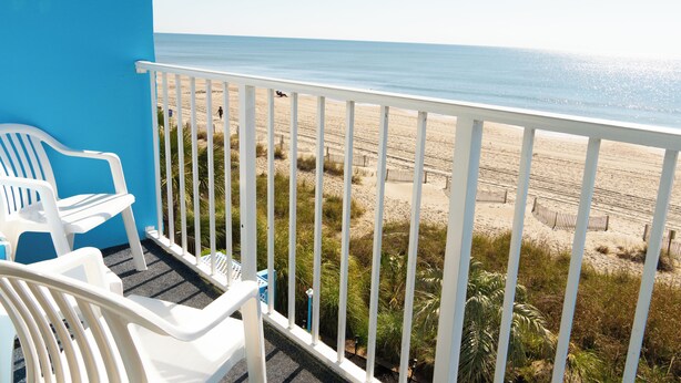 A balcony with white plastic chairs and a view of the beach. - Beach Club at Montego Inn (Myrtle Beach)