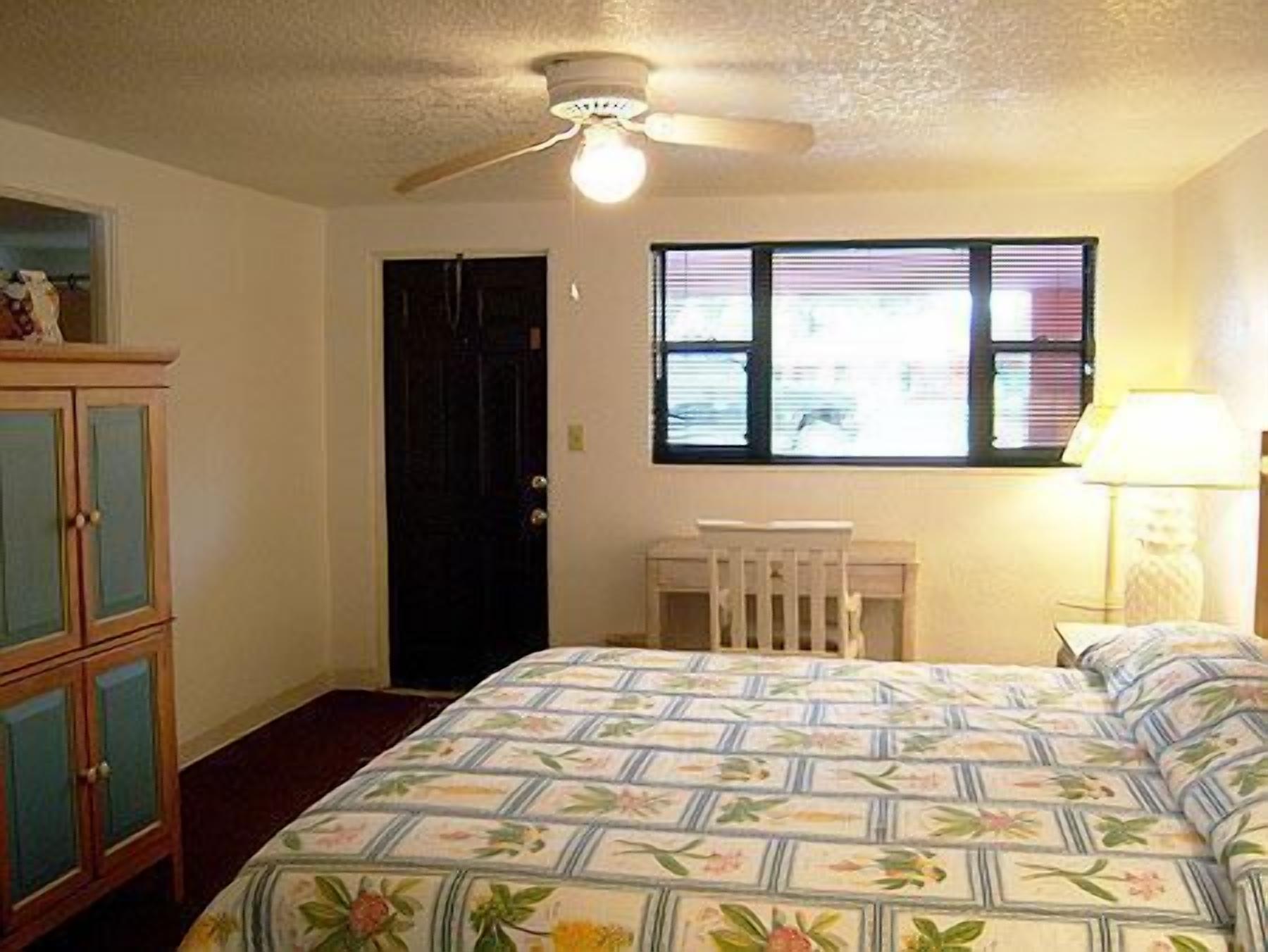 A bedroom with a bed, a window with blinds, a ceiling fan, and a dresser.