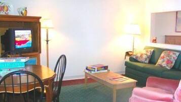 A living room with a television, a table, a couch, and a chair.