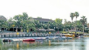 Marina com barcos atracados, rodeada por palmeiras e um edifício com área coberta.
