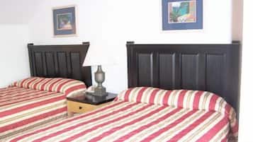 A hotel room with two beds, each with a dark headboard and striped bedding. There is a nightstand with a lamp between the beds.
