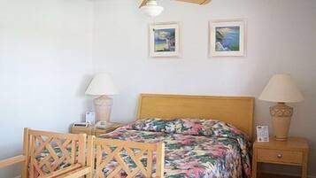 A bedroom with a wooden bed, two bedside tables with lamps, a ceiling fan, and two framed pictures on the wall.