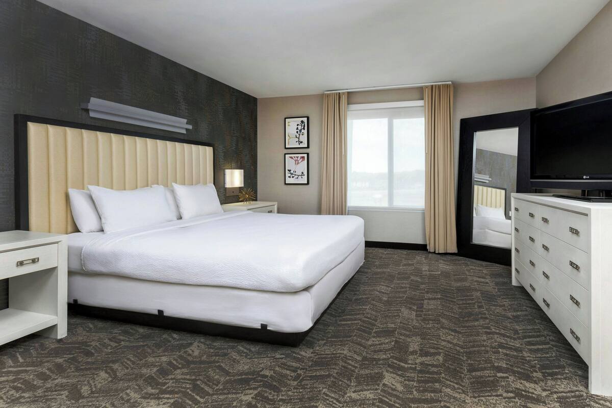 A hotel room with a large bed, a TV, a dresser, and a window with curtains.