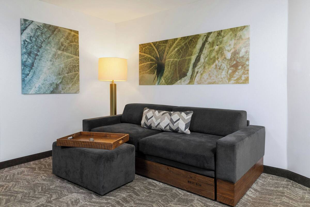 A modern living room with a grey sofa, a wooden side table, and two abstract paintings on the wall.