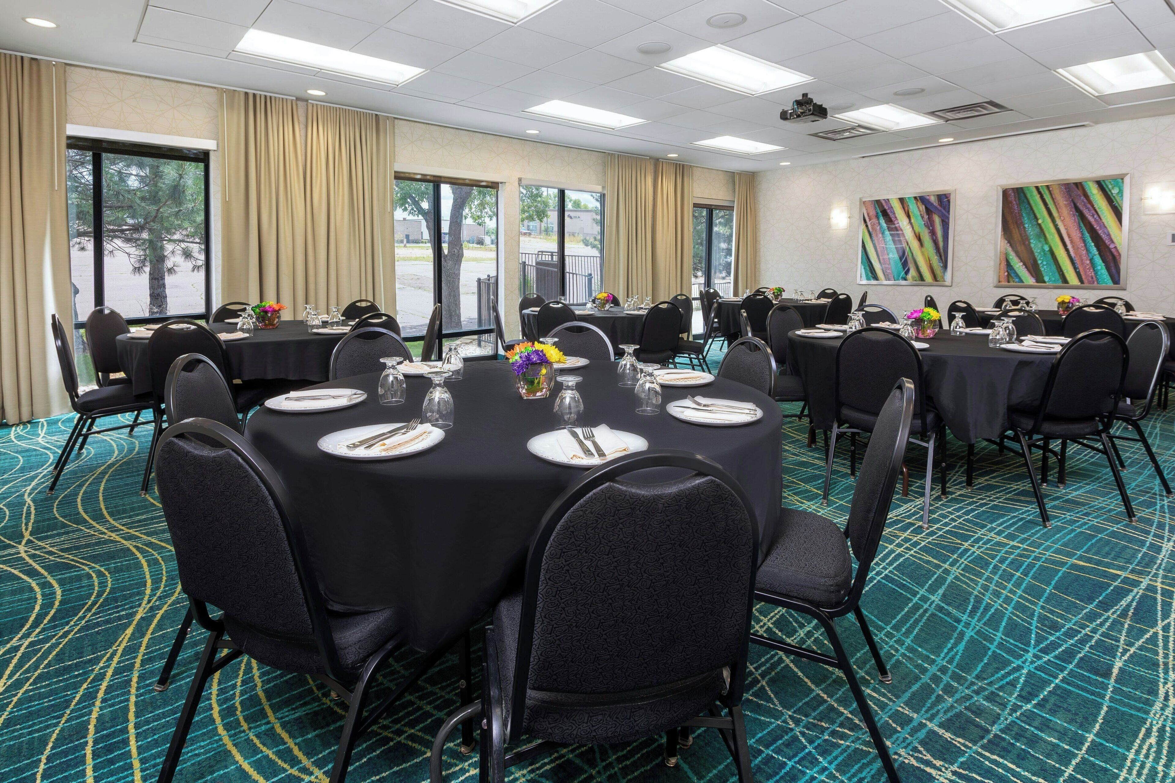 Un salón de conferencias con mesas redondas, sillas negras y una alfombra color turquesa.