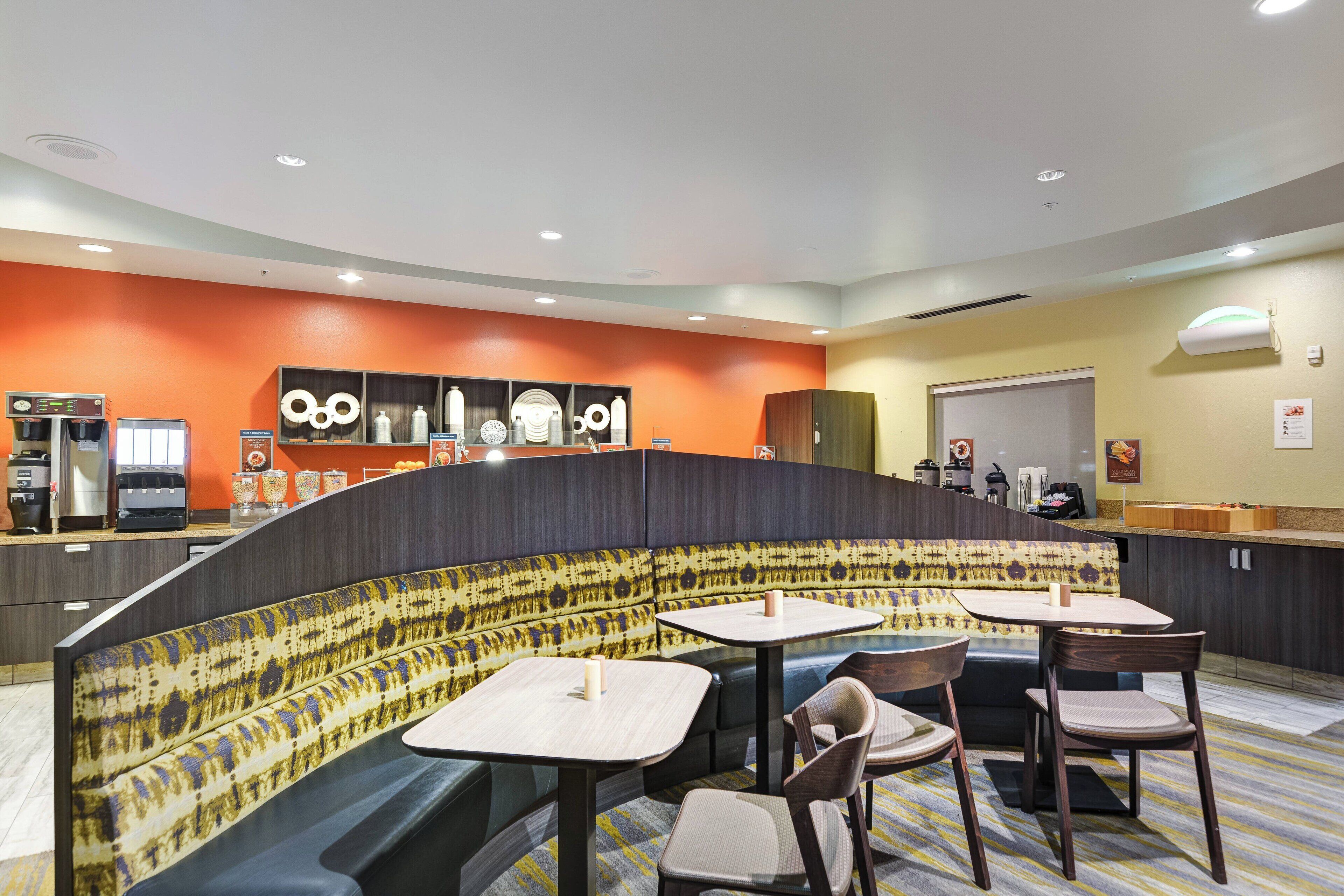Un restaurant moderne doté d’un espace salon aux lignes courbes, d’un comptoir avec une machine à café et d’un mur orné de motifs.