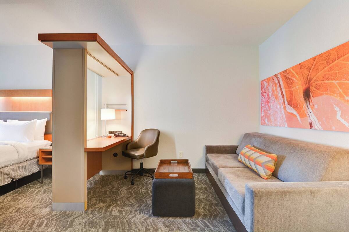 A hotel room with a bed, a desk, a chair, a sofa, and a large painting on the wall.