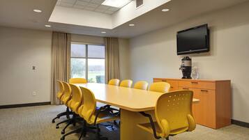 A conference room with a long table, yellow chairs, a television on the wall, and a coffee machine.