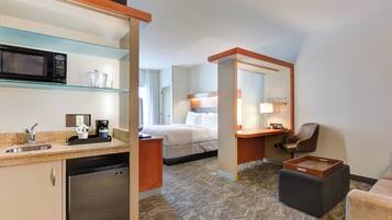 Une chambre d’hôtel équipée d’une kitchenette, d’un lit, d’un bureau, d’une chaise et d’un petit pouf.
