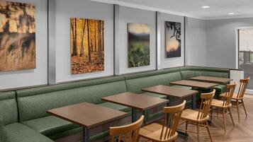 A restaurant with a green cushioned bench seating, wooden tables, and artwork on the walls.