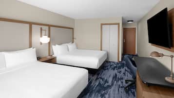 Habitación de hotel con dos camas, un escritorio, una silla, un televisor y una lámpara.