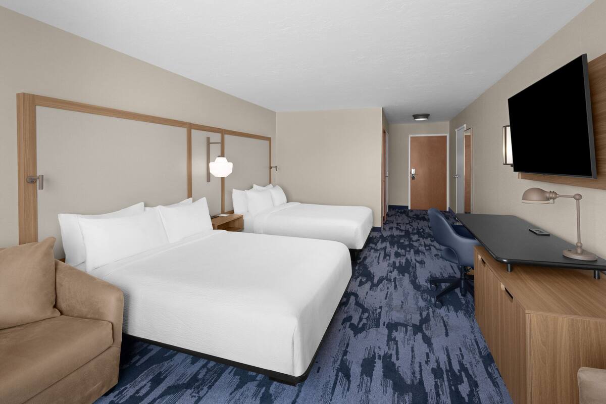 A hotel room with a large bed, a smaller bed, a desk with a computer, a TV, and a sofa.