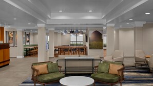 Un lobby amplio con mostrador de recepción, zona de estar con sofás y sillones, comedor con mesas y sillas, y un ventanal con vistas.