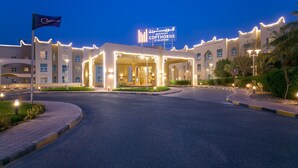 Una entrada de hotel con un letrero iluminado de gran tamaño, una bandera y un camino de acceso bien iluminado.