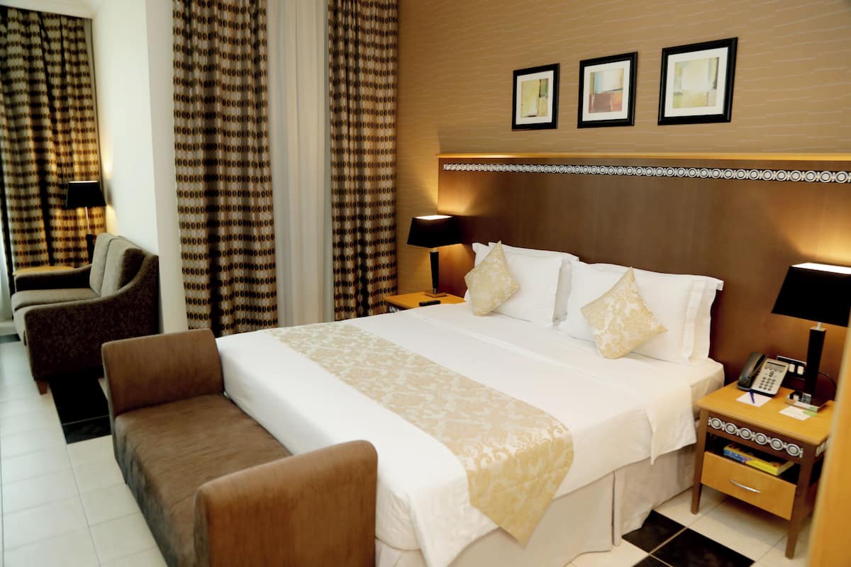 A hotel room with a large bed, a bedside table with a lamp, a chair, and curtains.
