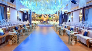 Un salón amplio y elegantemente decorado, con un escenario central, asientos a ambos lados y elementos decorativos colgantes.
