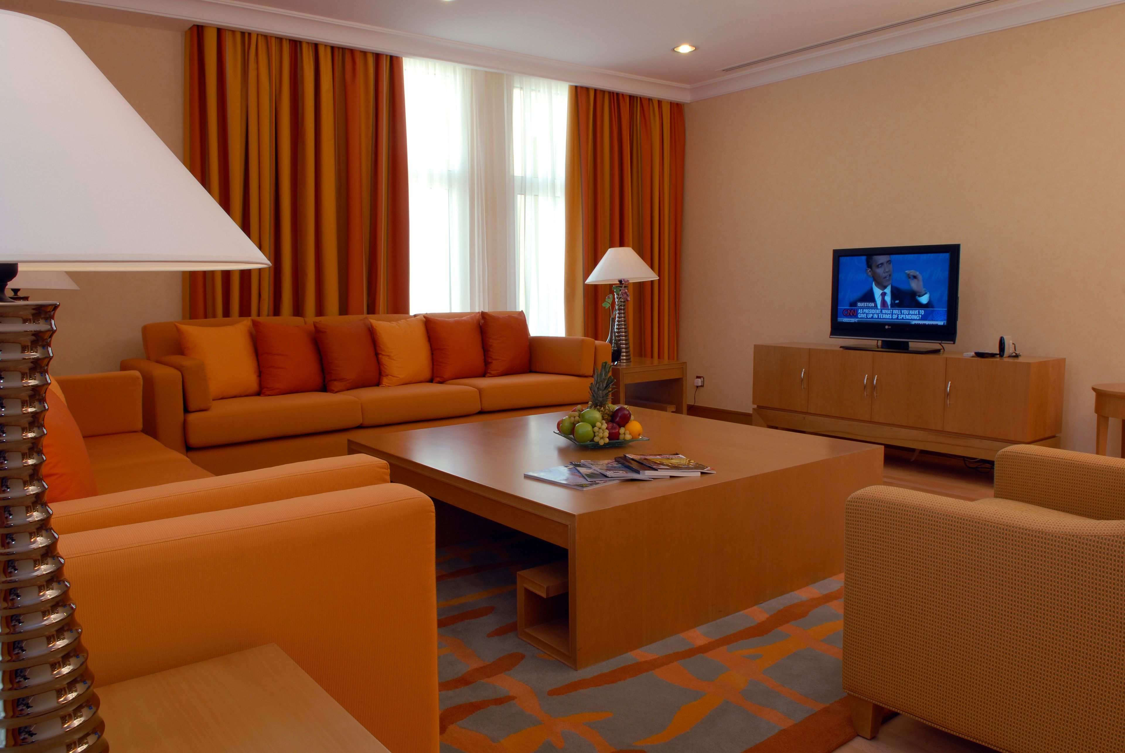 Ein modernes Wohnzimmer mit orangefarbenen Möbeln, einem Couchtisch mit Zeitschriften und Früchten, einem Fernseher und einer Lampe.