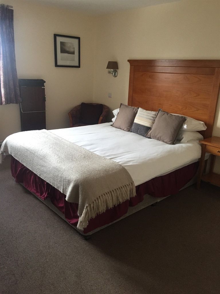 A standard hotel room with a large bed, a wooden headboard, a bedside table, and a chair.