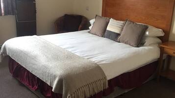 A standard hotel room with a large bed, a wooden headboard, a bedside table, and a chair.
