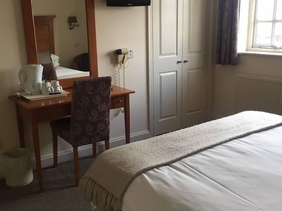 Une chambre d’hôtel comprenant un lit, un bureau avec une chaise, une télévision, un miroir et une fenêtre avec des rideaux.